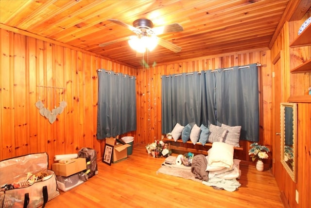 interior space with ceiling fan, wooden ceiling, light hardwood / wood-style floors, and wood walls