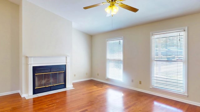 unfurnished living room with ceiling fan, baseboards, a fireplace with flush hearth, and wood finished floors