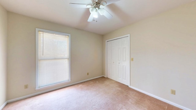 unfurnished bedroom featuring a closet, baseboards, light colored carpet, and ceiling fan