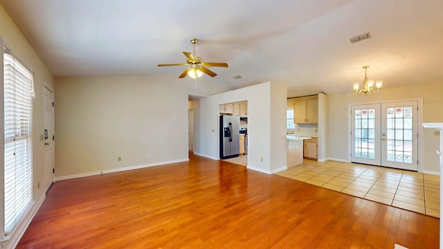 unfurnished living room featuring visible vents, light wood finished floors, vaulted ceiling, french doors, and ceiling fan with notable chandelier