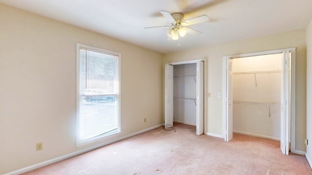 unfurnished bedroom with light colored carpet, baseboards, two closets, and ceiling fan