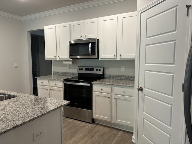 kitchen with hardwood / wood-style flooring, white cabinetry, stainless steel appliances, light stone countertops, and ornamental molding