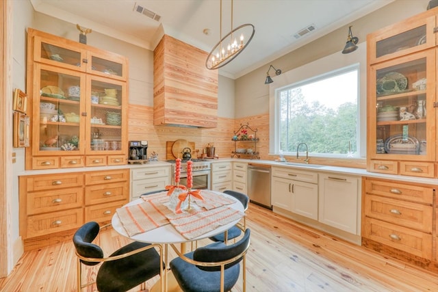 kitchen with appliances with stainless steel finishes, sink, white cabinets, hanging light fixtures, and light hardwood / wood-style flooring