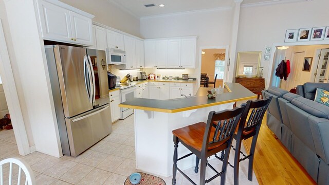 kitchen featuring light tile patterned floors, white appliances, crown molding, a breakfast bar, and white cabinetry