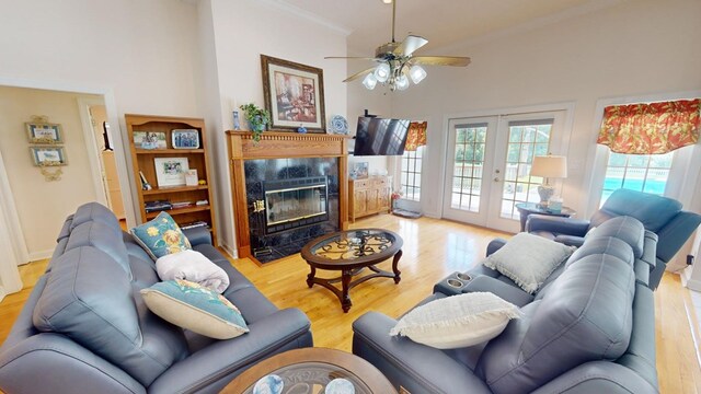 living room featuring ceiling fan, a fireplace, ornamental molding, french doors, and light wood-type flooring