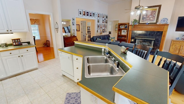 kitchen with sink, light tile patterned floors, a tile fireplace, dishwasher, and white cabinets