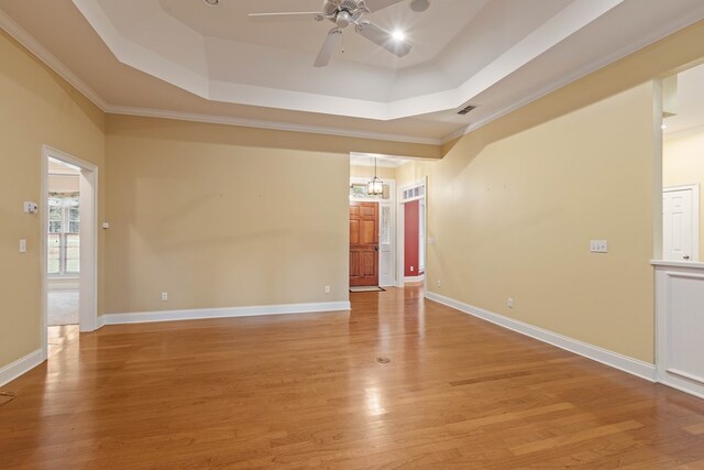 spare room featuring crown molding, a tray ceiling, ceiling fan, and light wood-type flooring