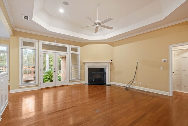 unfurnished living room with hardwood / wood-style floors, a tray ceiling, ornamental molding, and french doors