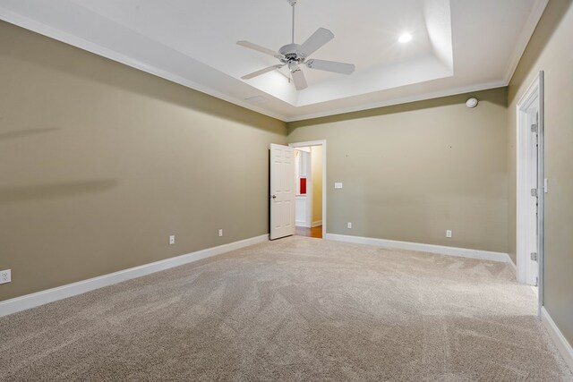 unfurnished bedroom with ceiling fan, light colored carpet, ornamental molding, and a tray ceiling