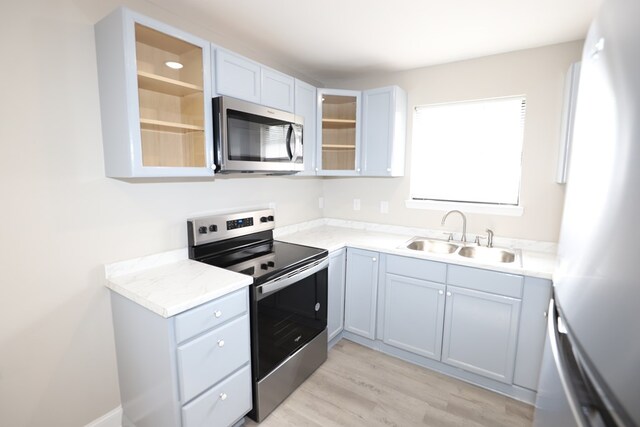 kitchen with appliances with stainless steel finishes, light stone countertops, sink, and light hardwood / wood-style flooring