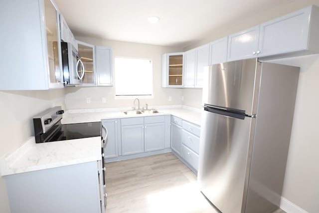 kitchen with light stone counters, sink, light hardwood / wood-style flooring, and appliances with stainless steel finishes