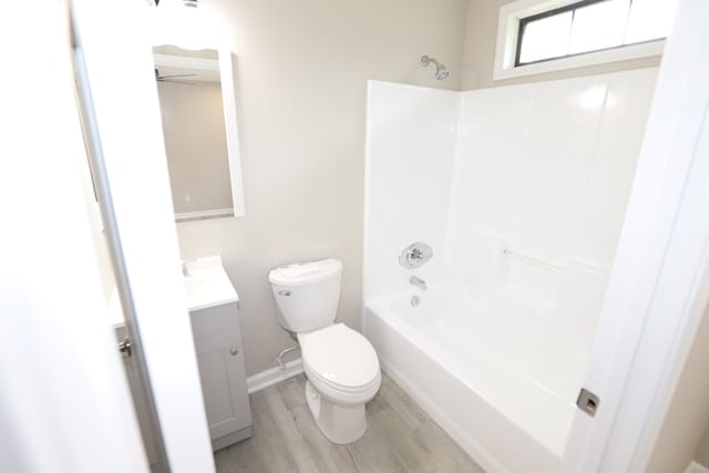 full bathroom with hardwood / wood-style flooring, washtub / shower combination, vanity, and toilet