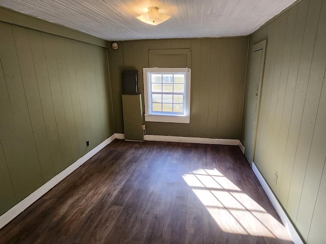 empty room featuring electric panel, baseboards, and wood finished floors