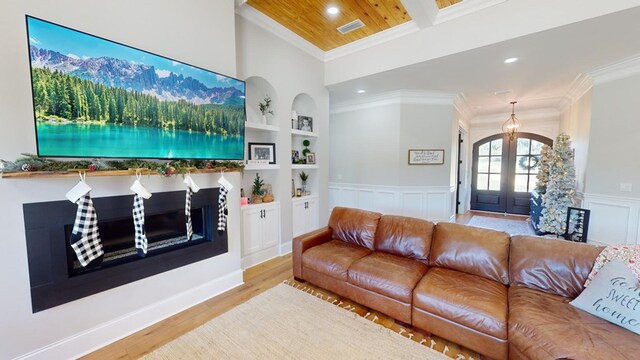 living room featuring built in shelves, ornamental molding, light hardwood / wood-style flooring, and french doors