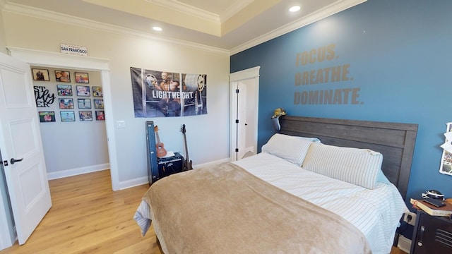 bedroom with ornamental molding, a tray ceiling, and light hardwood / wood-style flooring