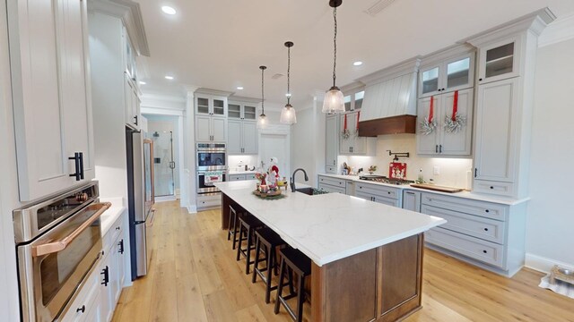 kitchen featuring sink, a breakfast bar, premium range hood, a center island with sink, and decorative light fixtures