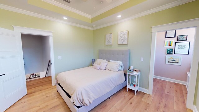 bedroom featuring a raised ceiling, ornamental molding, and light wood-type flooring