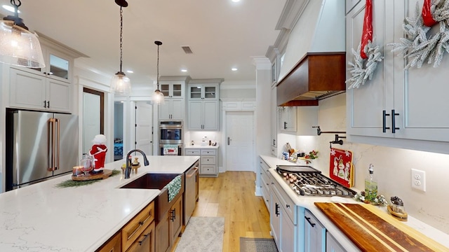 kitchen with appliances with stainless steel finishes, decorative light fixtures, sink, ornamental molding, and light hardwood / wood-style flooring