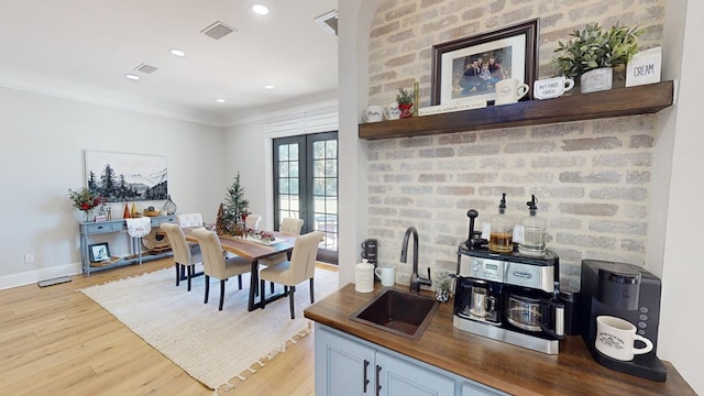 dining area with crown molding, sink, light wood-type flooring, and french doors