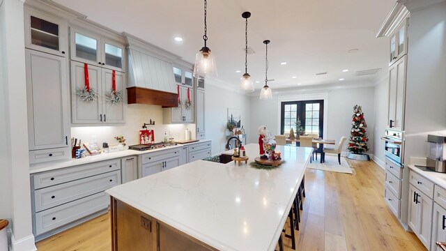 kitchen with a large island, sink, pendant lighting, light stone countertops, and light wood-type flooring