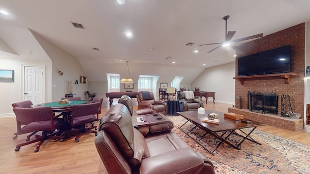 living area featuring lofted ceiling, light wood-style flooring, a ceiling fan, baseboards, and a brick fireplace