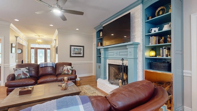 living room with wood finished floors, ceiling fan, a fireplace, built in features, and crown molding