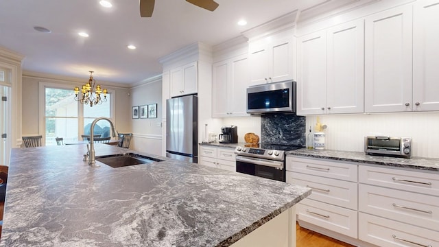 kitchen featuring stainless steel appliances, a sink, white cabinets, a chandelier, and a ceiling fan