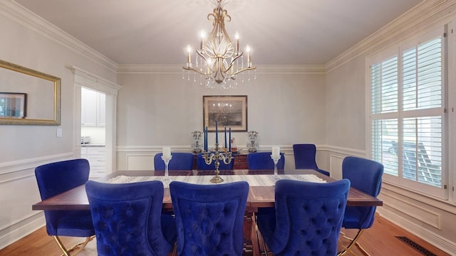 dining area featuring a chandelier, healthy amount of natural light, crown molding, wood finished floors, and a decorative wall