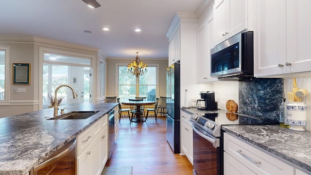 kitchen with stainless steel appliances, a sink, light wood-style flooring, decorative backsplash, and white cabinets