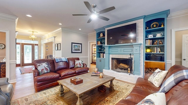 living room featuring light wood finished floors, ceiling fan, a brick fireplace, built in shelves, and crown molding