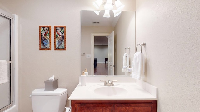full bath featuring vanity, toilet, a shower with door, and a textured wall