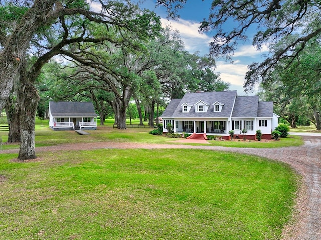 cape cod home with covered porch, curved driveway, a front yard, and an outbuilding