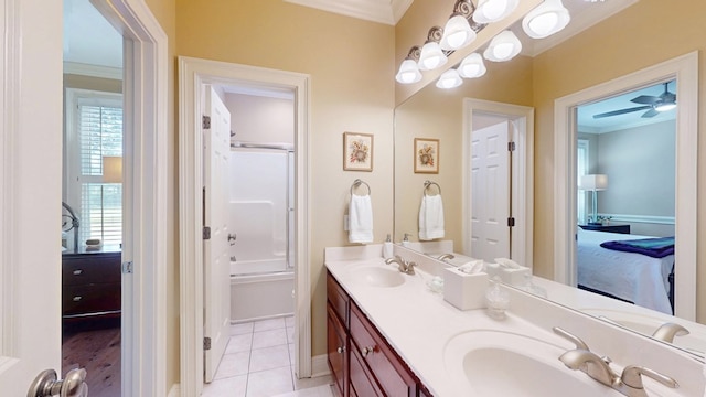 ensuite bathroom with ornamental molding, double vanity, ceiling fan, baseboards, and bath / shower combo with glass door