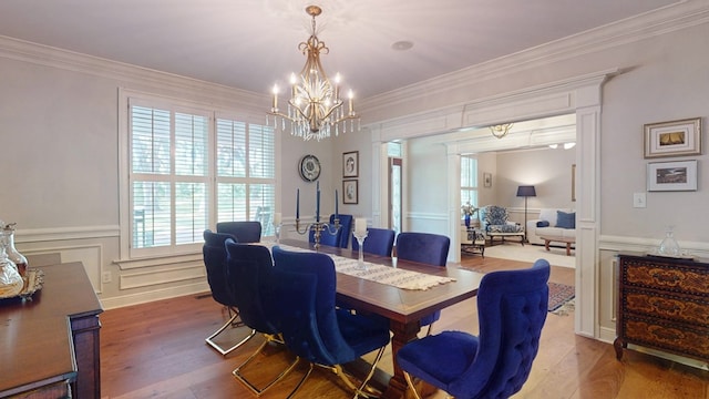 dining room with a chandelier, wood finished floors, ornamental molding, a wainscoted wall, and a decorative wall