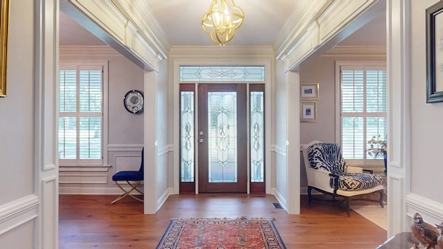 foyer entrance with a chandelier, wood finished floors, crown molding, and a wainscoted wall
