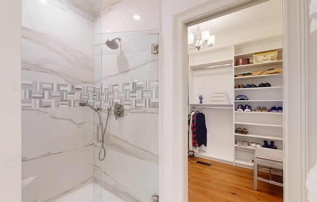 bathroom with a marble finish shower, a walk in closet, wood finished floors, and a chandelier