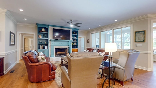 living room featuring a brick fireplace, ceiling fan, light wood-style floors, baseboards, and crown molding