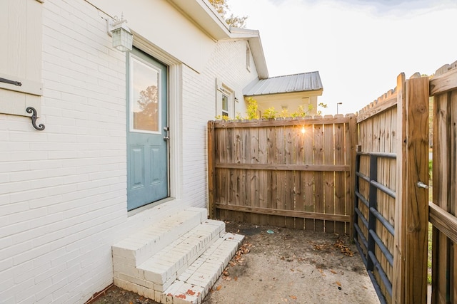 view of exterior entry featuring brick siding, fence, and metal roof