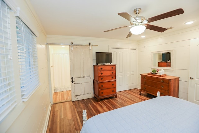 bedroom featuring ornamental molding, a barn door, a ceiling fan, a closet, and wood finished floors