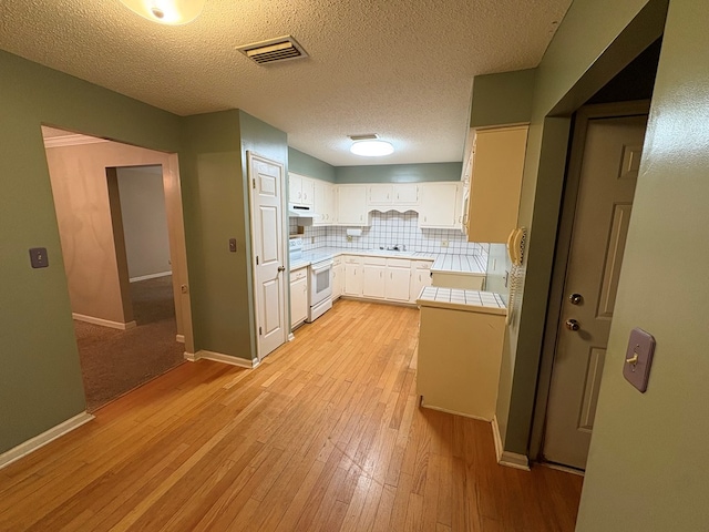 102 Spruce Pine Dr, Thomasville, GA 31757 - kitchen with light wood-style floors, backsplash, white cabinetry, under cabinet range hood, and tile countertops