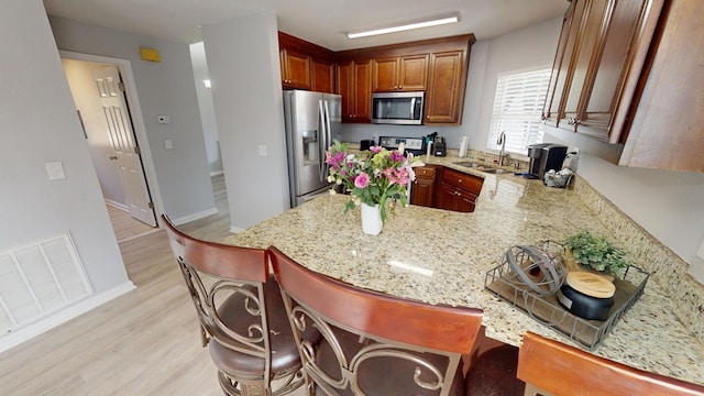 kitchen with sink, stainless steel appliances, light stone counters, light hardwood / wood-style floors, and kitchen peninsula