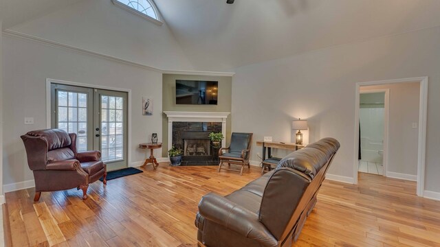 living room with high vaulted ceiling, a tile fireplace, light hardwood / wood-style floors, and french doors