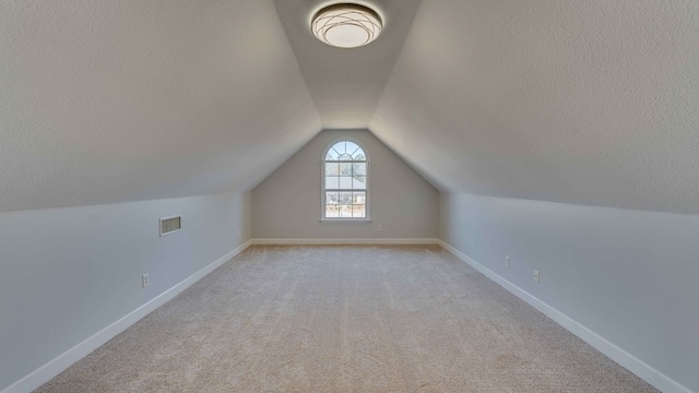 bonus room with light carpet, lofted ceiling, and a textured ceiling