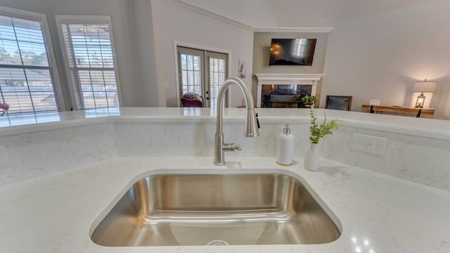 interior details with sink, decorative backsplash, a high end fireplace, light stone countertops, and french doors