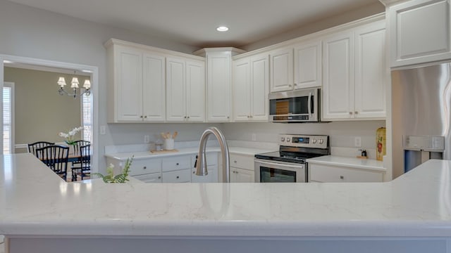 kitchen featuring sink, white cabinetry, stainless steel appliances, light stone countertops, and a chandelier