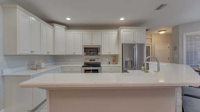 kitchen featuring white cabinetry, light stone counters, stainless steel appliances, and a center island with sink