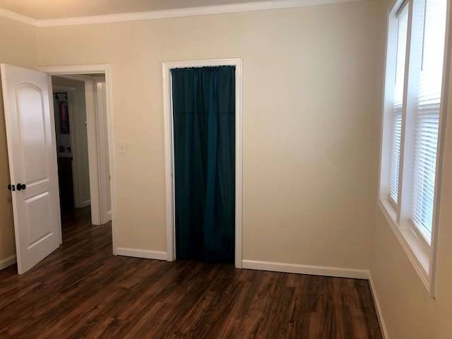 unfurnished bedroom featuring multiple windows, baseboards, dark wood finished floors, and ornamental molding