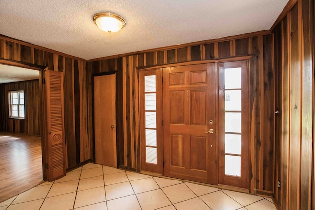foyer featuring a textured ceiling, wood walls, and light tile patterned floors