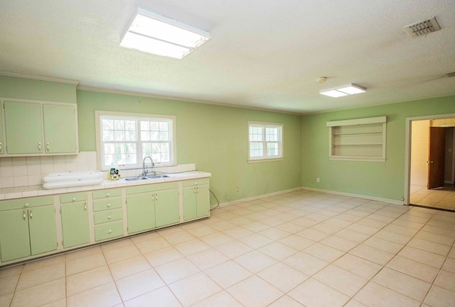 kitchen featuring a textured ceiling, visible vents, tile counters, built in shelves, and a sink