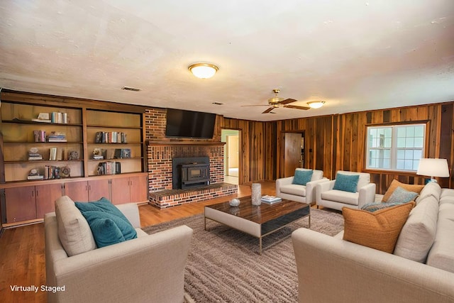 living room featuring a ceiling fan, wood finished floors, a wood stove, and wooden walls